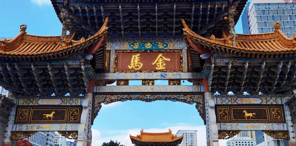 Kunming Jinma Biji Archway 昆明金馬碧雞坊矗立於廣場,藍天下的傳統建築展現飛簷翹角與精美彩繪。牌坊刻有「金馬」字樣,與後方現代城市建築交織。