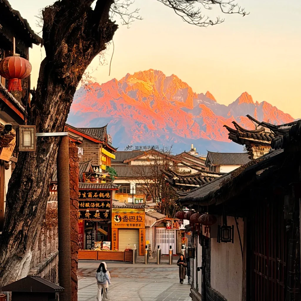 Lijiang Old Town 清晨的 麗江古城,傳統瓦屋、靜謐石板巷道,遠方是被晨光染金的玉龍雪山。
