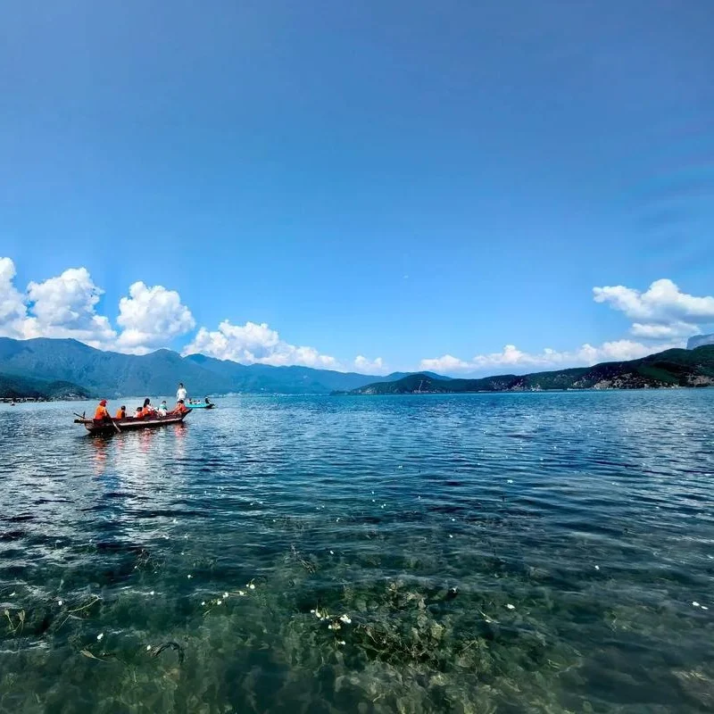 瀘沽湖的經典畫面：澄澈湖水、豬槽船與水面上的水性楊花，搭配藍天白雲與遠山，宛如人間仙境。