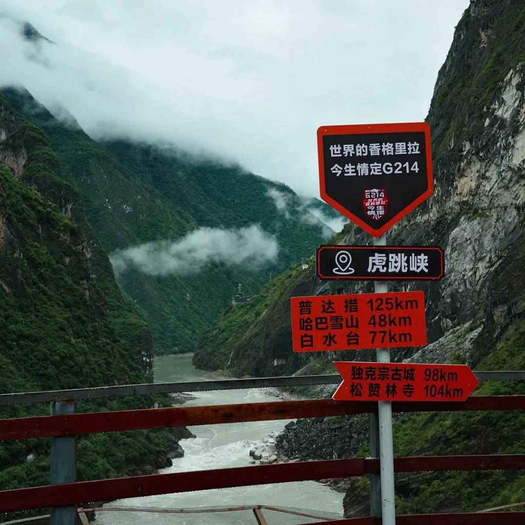 Upper Tiger Leaping Gorge Scenic Area 1 壯麗的 香格里拉虎跳峽 景色,翠綠峽谷被雲霧環繞,下方金沙江奔流,前方設有觀景路牌。