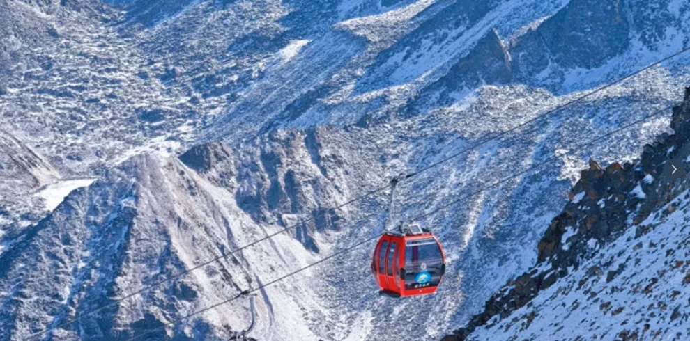 cableway 雲南麗江玉龍雪山冰川公園大索道的高山纜車景觀。紅色纜車在高空運行,穿越壯麗的雪山與冰川山脈,遠處連綿山峰覆蓋著白雪。崎嶇山脊與冰雪地貌展現高原壯觀景色,整個畫面呈現出震撼的自然風光與著名的高山旅遊體驗。
