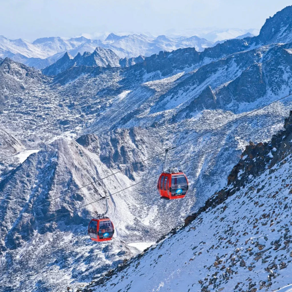 cableway 雲南麗江 玉龍雪山冰川公園大索道 的高山纜車景觀。紅色纜車在高空運行,穿越壯麗的雪山與冰川山脈,遠處連綿山峰覆蓋著白雪。崎嶇山脊與冰雪地貌展現高原壯觀景色,整個畫面呈現出震撼的自然風光與著名的高山旅遊體驗。