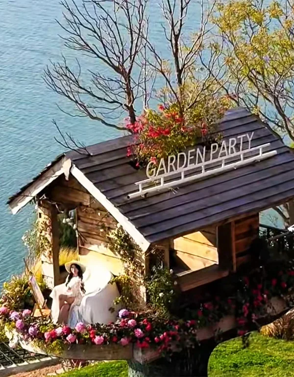 Slow Living in a Dali Erhai Log Cabin 大理洱海小木屋慢生活場景,湖畔木屋環繞花卉,一人悠閒享受寧靜時光。