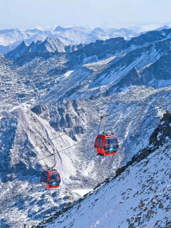 cableway 雲南麗江玉龍雪山冰川公園大索道的高山纜車景觀。紅色纜車在高空運行,穿越壯麗的雪山與冰川山脈,遠處連綿山峰覆蓋著白雪。崎嶇山脊與冰雪地貌展現高原壯觀景色,整個畫面呈現出震撼的自然風光與著名的高山旅遊體驗。